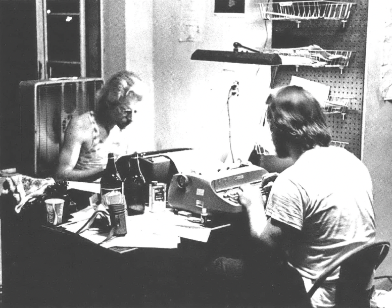 Two men at a desk, typing on typewriters