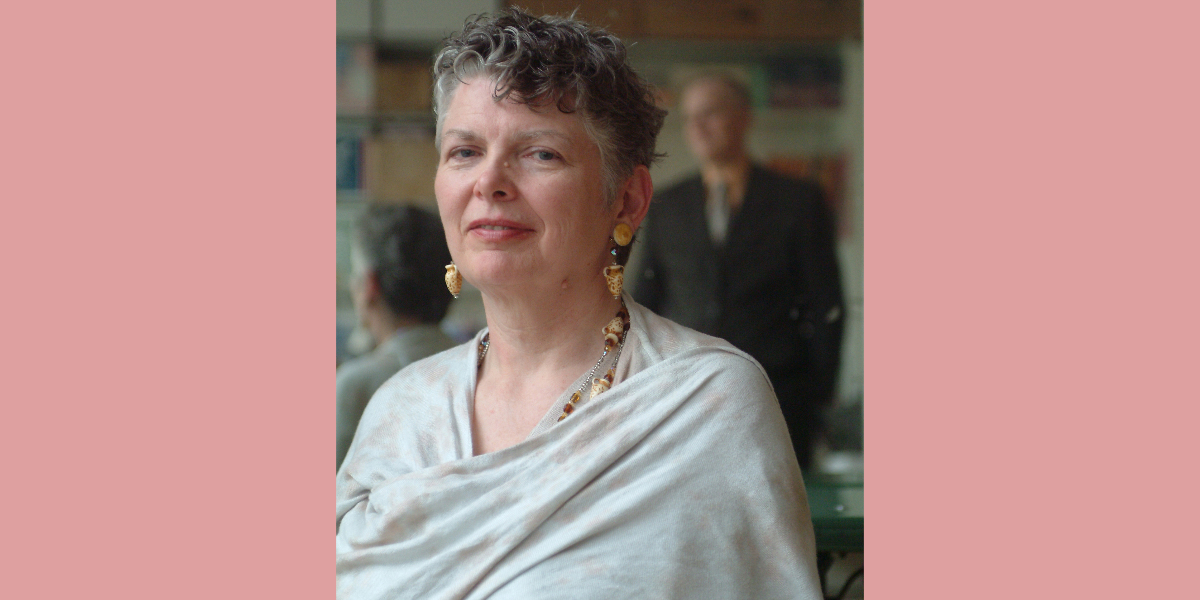 A portrait of a woman with short grey hair smiling softly at the camera, against a soft pink background