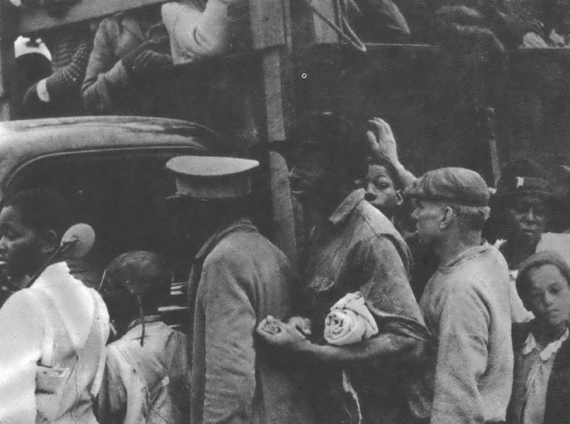 Black and white migrants crowding around a truck full of migrants