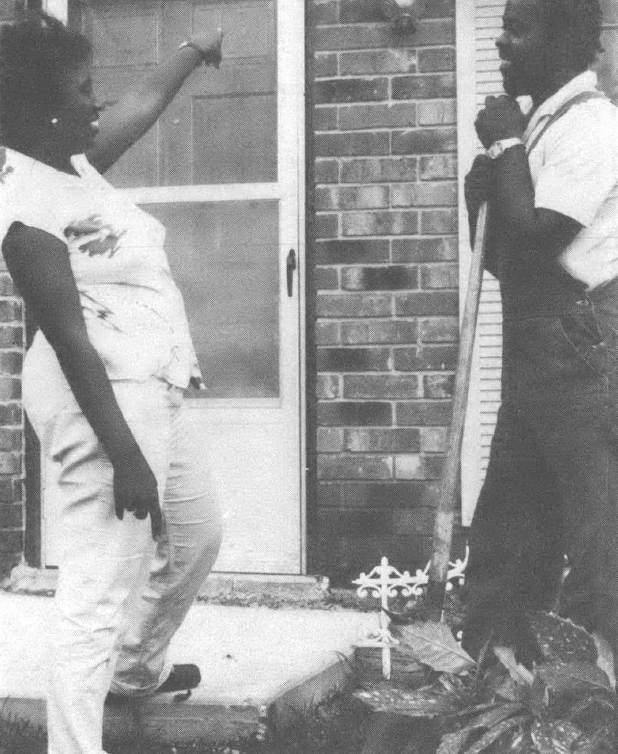 Black and white photo of people talking and laughing in front of a house