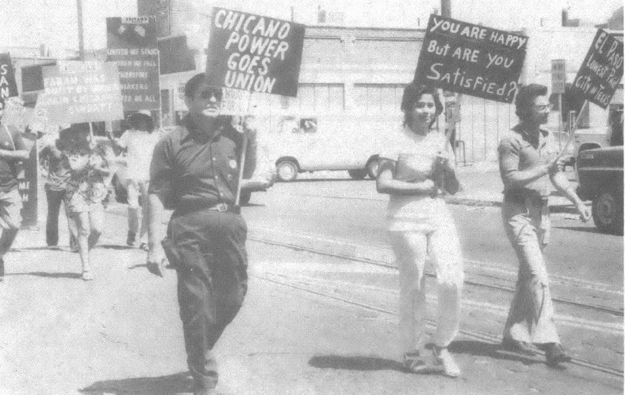 Black and white photo of people marching down street with signs