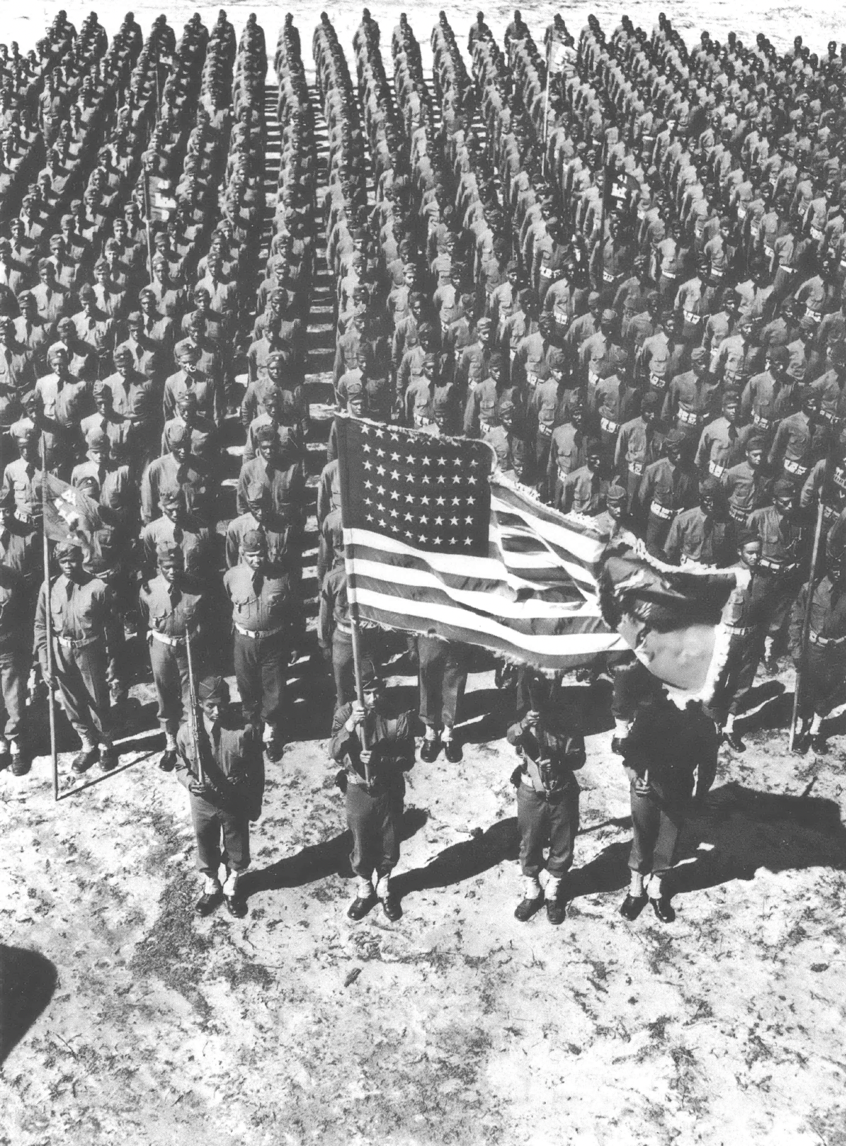 Black and white photo of rows of soldiers with an American flag in front