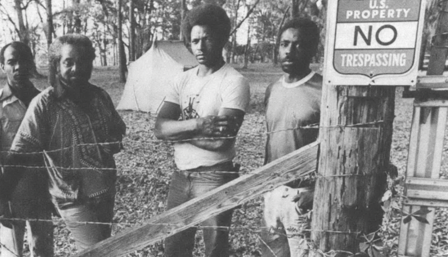 Men standing behind a fence and no trespassing sign