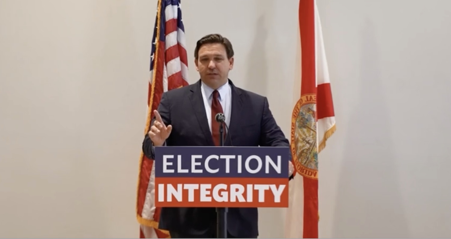 Florida Gov. Ron DeSantis speaking at a podium with a sign on it saying "election integrity"