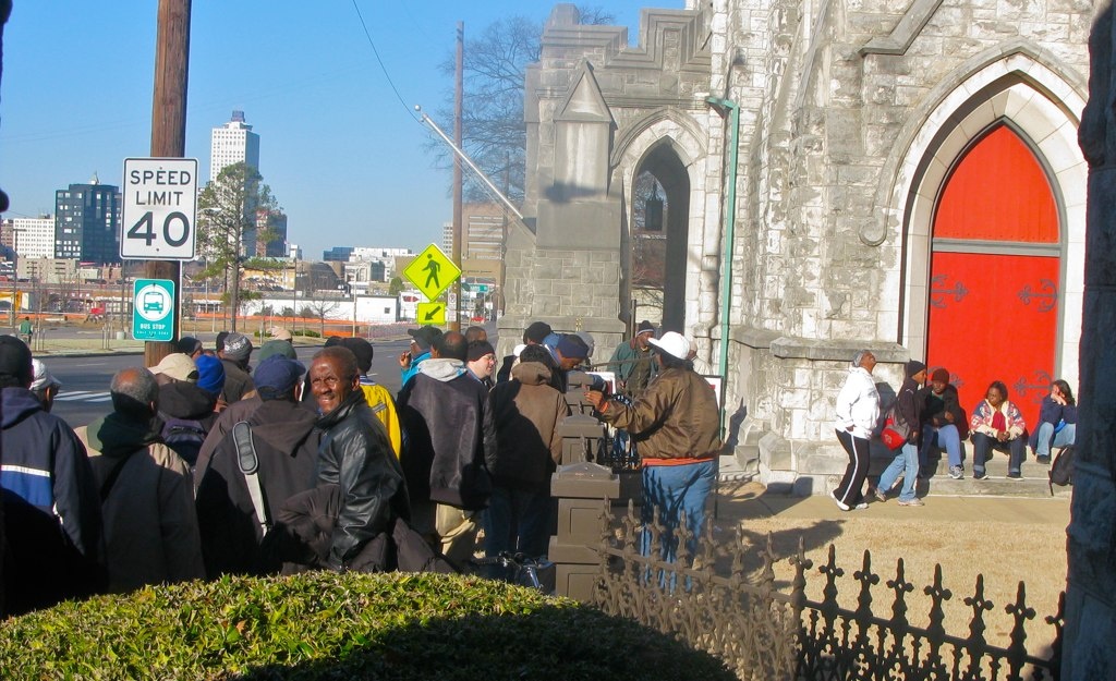 People stand in line outside a stone church with a bright red door