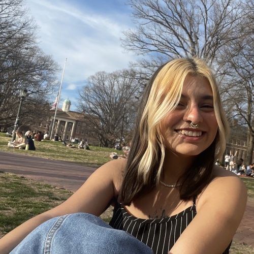 Photo of woman with blonde and brunette hair sitting on grass and smiling