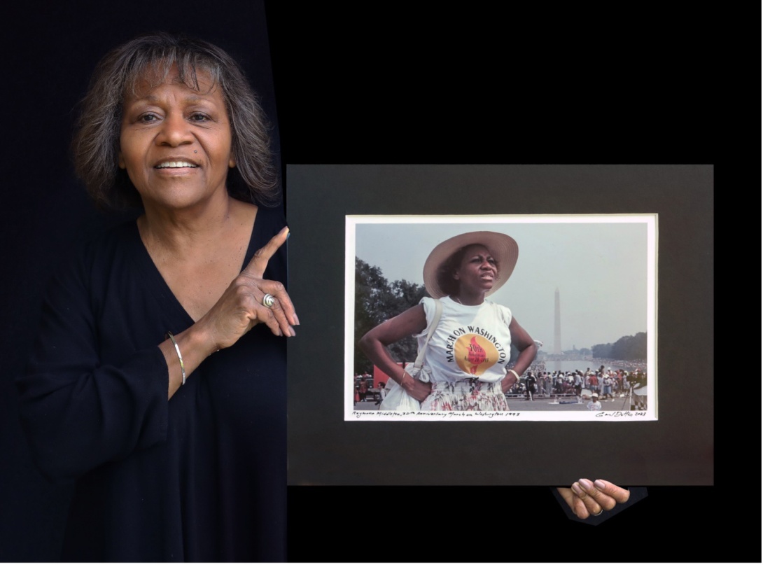 Recent photograph of Raymona Middleton holding a large photograph of herself at the March on Washington thirty years ago, against a black background