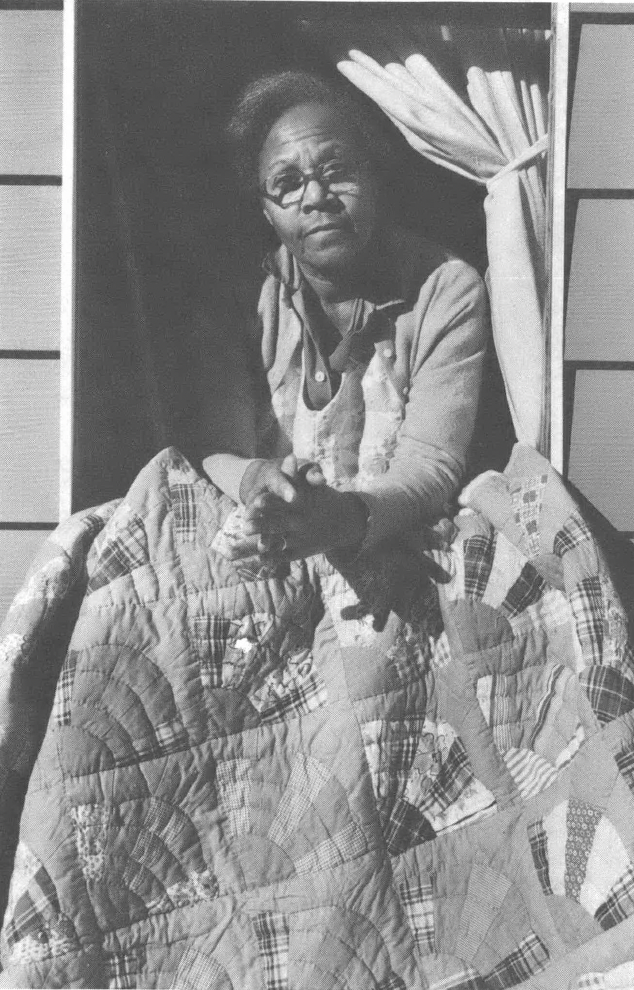 Black and white photo of Black woman with quilt in doorway 