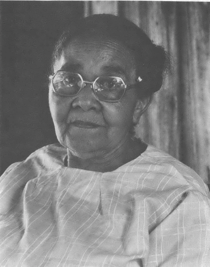 Black and white portrait photo of Black woman wearing glasses, hair pulled back, and light-colored top