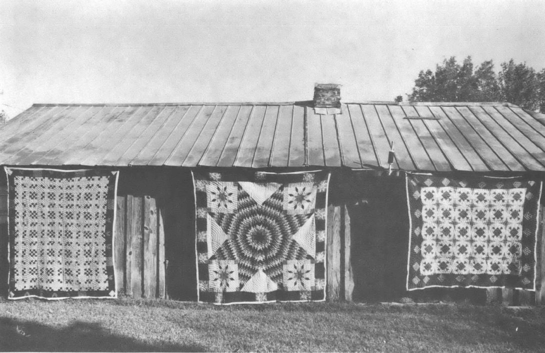 Black and white photo of quilts hanging off of building
