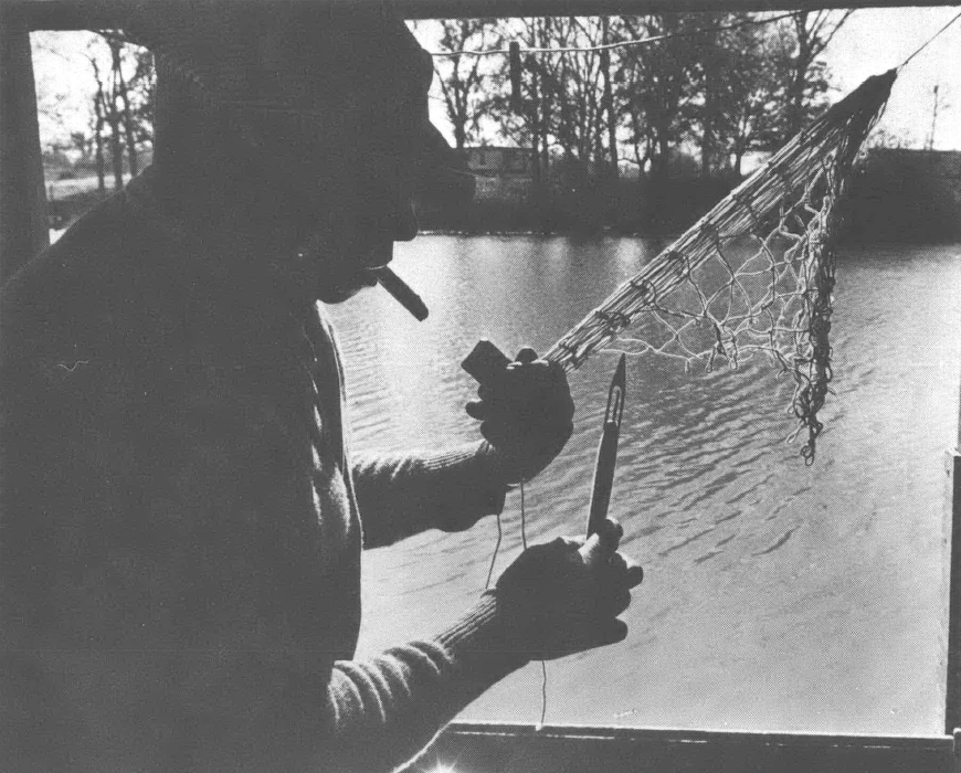 Black and white photo of man cutting net in front of a window