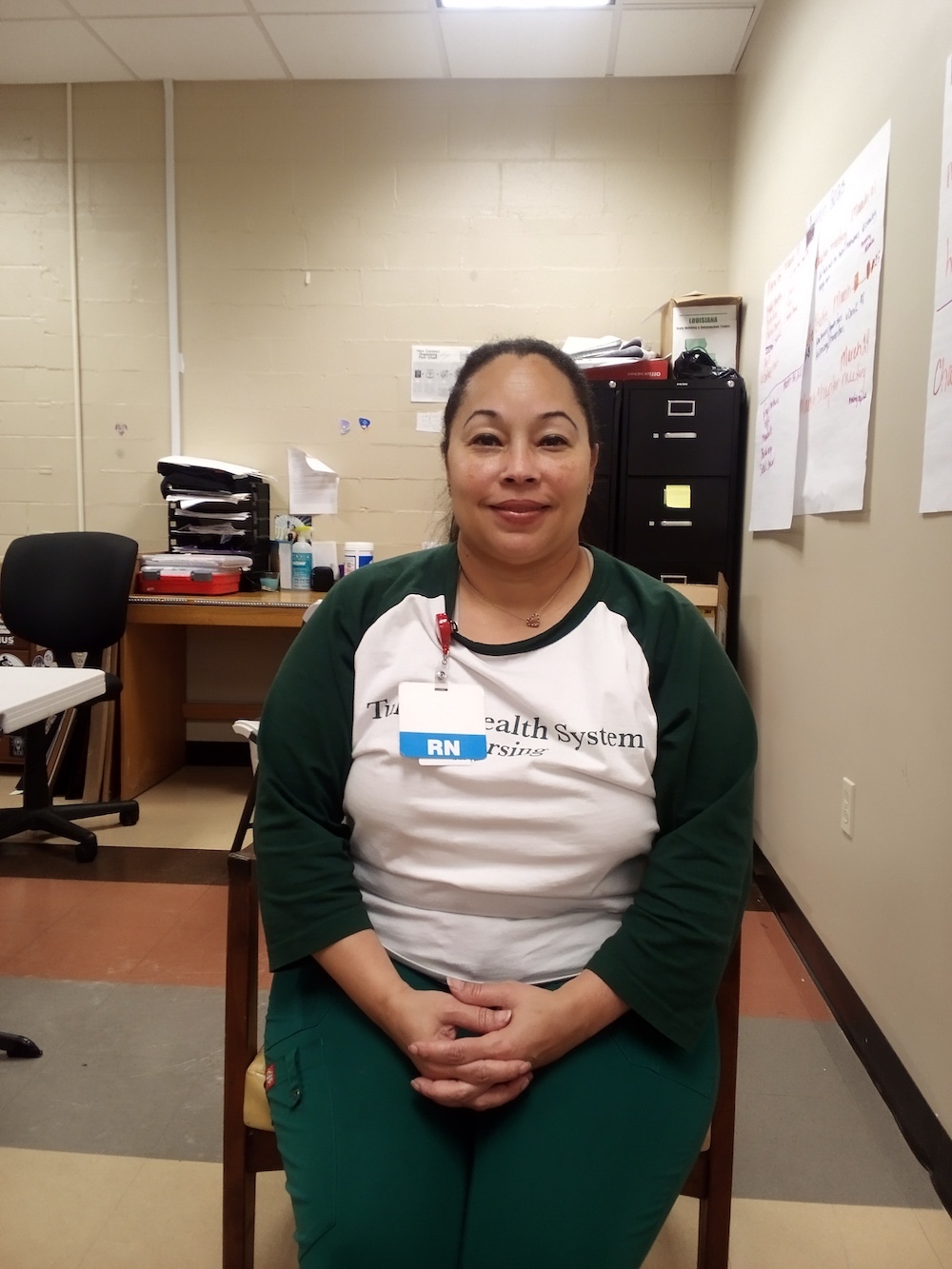 Woman wearing Tulane T-shirt and RN tag, sitting in chair and smiling at the camera