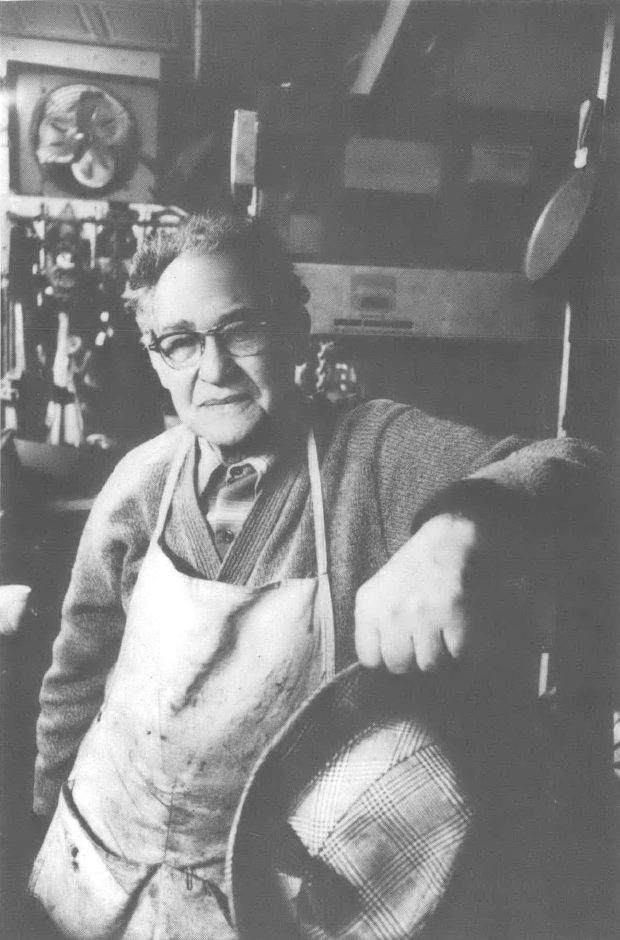 Black and white photo of white man in glasses leaning against a wall