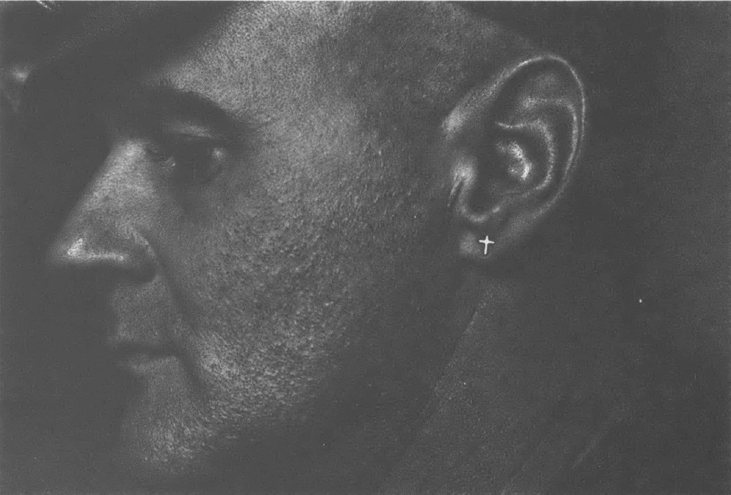 Black and white side profile of white man with stubble and cross stud earring