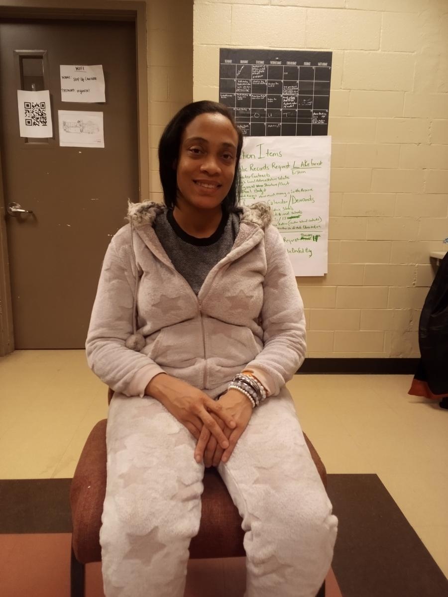 Black woman in a sweat suit sitting in a chair, looking at the camera and smiling
