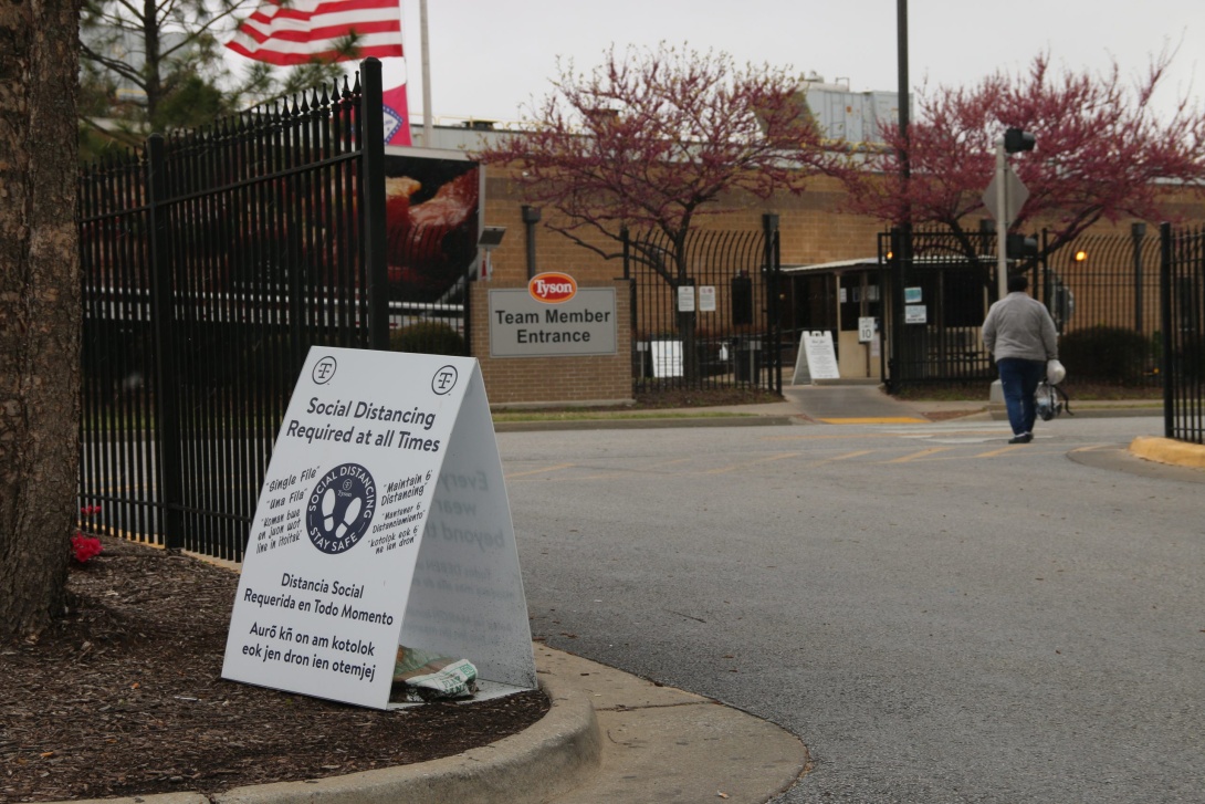 A Tyson employee walks into the team member entrance at the Berry Street location in Springdale, Arkansas. A sign in their path read "Social Distancing Required at all Times" written in English, Spanish and Marshallese.