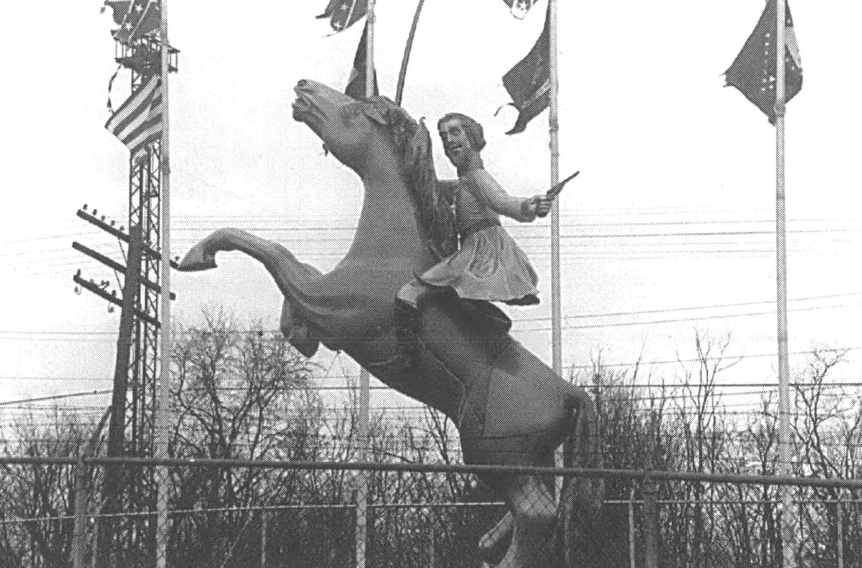 A black and white photo of a statue of a man on a horse, surrounded by several tattered flags, including Confederate flags.