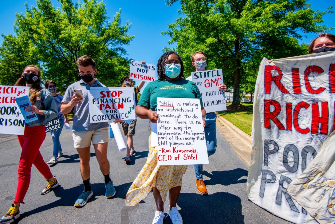 Several people walking down a street holding signs in protest of Alabama's prison lease plan