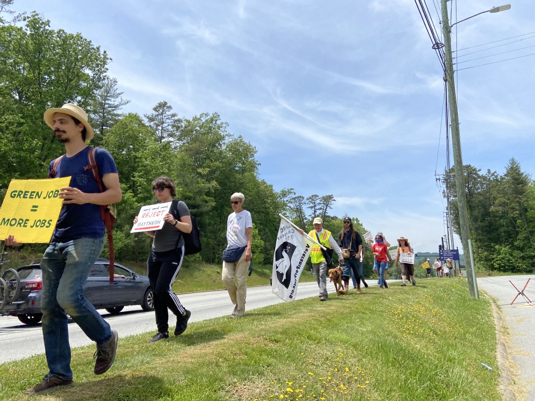 A line of marchers holding signs alongside a highway.